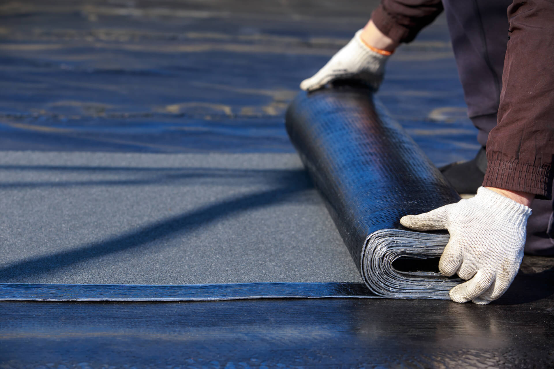 Roofer rolling out SBS modified bitumen membrane during a flat roof installation