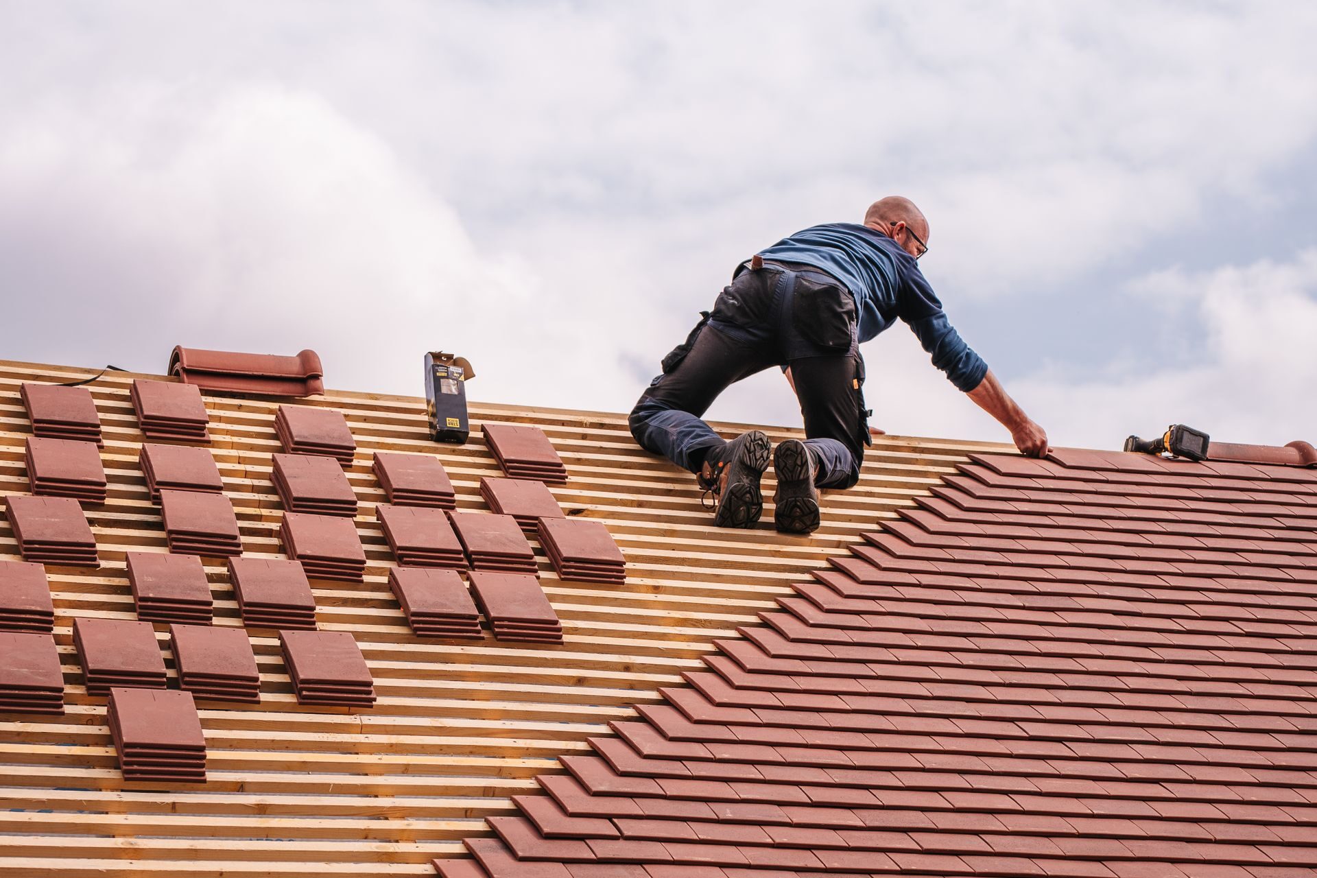 Roofer setting new clay tiles on wooden battens during a tile roof installation