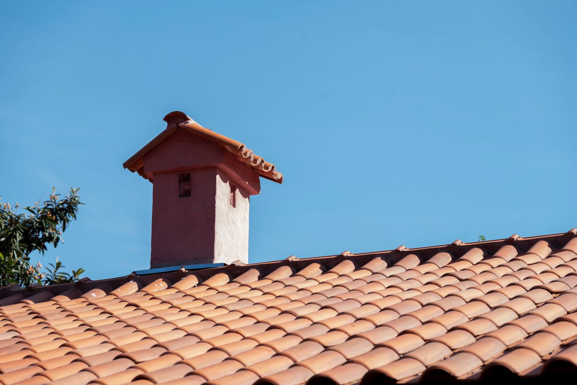 Clay_Tile_Ridge_Hip_Flashing_Repair Chimney and ridge line on a clay tile roof against a blue sky